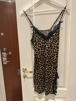 Leopardmönstrat nattlinne med spets - Snyggt nattlinne med leopardmönster och svarta spetsdetaljer vid halsringning och slits. Tunt axelbandslinne i mjukt, glansigt material som ger en lyxig känsla. Perfekt för dig som gillar djurmönster och vill ha något extra till natten. Passar en xs/s beroende på hur man vill den ska sitta