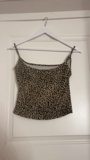 Leopardmönstrad linnetopp - Säljer en snygg leopardmönstrad linnetopp med smala axelband. Toppen har en beige och brun färgton med svarta detaljer i mönstret. Perfekt för dig som vill sticka ut med ett djuriskt print. Materialet känns lätt och bekvämt mot huden.