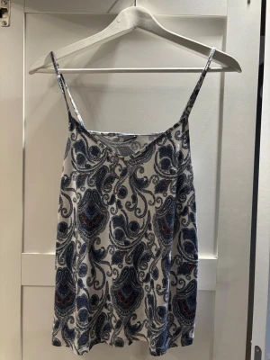 Mönstrad linnetopp från Gina Tricot - Säljer en snygg linnetopp från Gina Tricot i storlek M. Toppen har tunna axelband och ett paisleyinspirerat mönster i blått och vitt med små inslag av rött. Perfekt för varma dagar och enkel att matcha med jeans eller kjol.