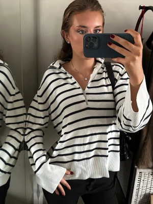 Vit och svart randig half zip tröja - Säljer en vit och svart randig tröja med half zip och hög krage. Tröjan har långa ärmar och är tillverkad i ett mjukt stickat material. Passformen är loose och den har breda muddar vid ärmslut och nederkant. Perfekt för dig som gillar en chill och stilren look.