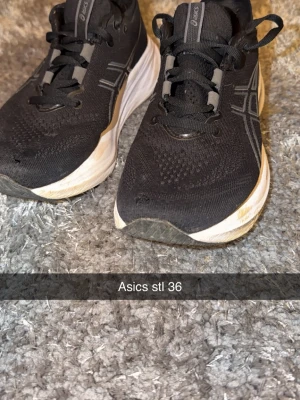 Svarta Asics sneakers strl 36 - Säljer ett par svarta Asics sneakers i storlek 36 med vita och grå detaljer. Skorna har snörning och en rund tå, samt en tjock, vit sula med PureGEL-dämpning. Ovandelen är i syntetmaterial med ventilerande mesh för extra komfort.