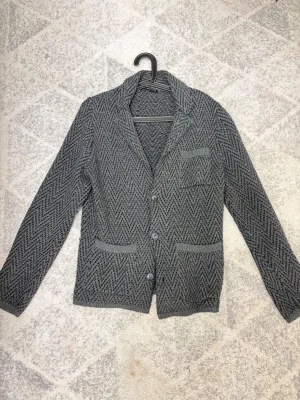 Grå stickad cardigan jacka med mönster - Snygg grå stickad cardigan jacka från Defacto Studio med zigzag-mönster. Jackan har tre framfickor, knappar framtill och en mjuk, skön känsla. Perfekt för dig som gillar en chill och stilren look med lite extra edge. Frakt görs samma dag som beställning!  Storlek S kan passa M beroende på längd