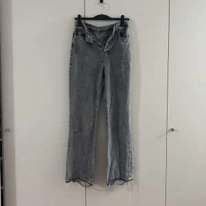 Grå wide jeans f - Säljer ett par gråa jeans med wide fit och hög midja. Jeansen har slitna och fransiga benslut för en cool, avslappnad vibe. Klassisk femficksmodell med knappgylf och Levis-lapp bak i midjan. Perfekta för dig som gillar loose och trendig stil. Slitningen längst ner är för klacken