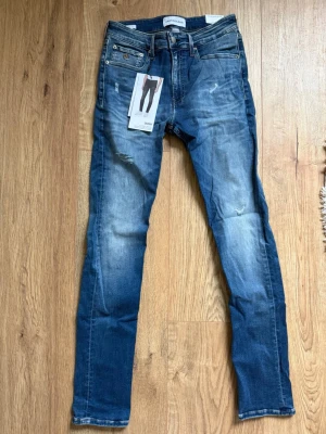 Calvin Klein skinny jeans blå storlek 30/32 - Snygga blå skinny jeans från Calvin Klein med klassisk femficksdesign och läderpatch bak. Jeansen har en lätt tvättad look med slitningar och sitter lågt i midjan. Materialet är mestadels bomull med lite polyester och elastan för stretch. Perfekta för en trendig och avslappnad stil. Nypris:1400kr