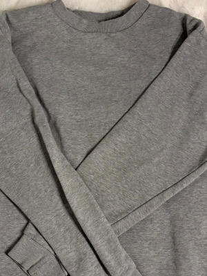 Grå sweatshirt med rund hals - En enkel och stilren grå sweatshirt med rund hals och långa ärmar. Tröjan har ribbade muddar vid ärmslut och nederkant, vilket ger en klassisk look. Perfekt för dig som gillar en clean och avslappnad stil.🤍