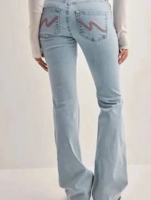 Low waist Nelly jeans med Rosa broderi på fickorna - Snygga ljusblå bootcut jeans från nelly med coolt rosa broderi på bakfickorna. Jeansen är lågmidjade och har dubbelknapp (se bild 4). Säljer pga av att de inte kommer till användning längre då jag har för många jeans. Skriv ifall ni har några frågor eller behöver flera bilder💗