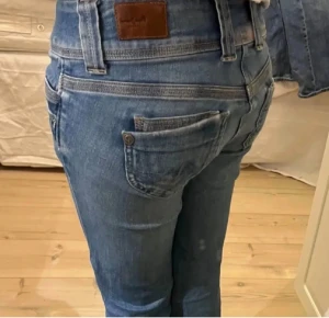 Blå Pepe Jeans Venus W28/L32 - Säljer ett par blå Pepe Jeans Venus med låg midja och raka ben. Jeansen har dubbla knappar fram, klassiska fickor och snygga detaljer vid linningen. Materialet är jeans med en mjuk känsla och passformen är normal. Perfekt för dig som gillar stilrena och coola jeans.