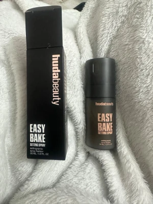 Huda Beauty Easy Bake Setting Spray - Easy Bake Setting Spray från Huda Beauty i en svart, matt flaska på 30 ml. Perfekt för att fixera sminket och ge en fräsch finish. Kommer i originalförpackning med stilren design och roséguldfärgad text.