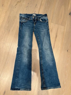 Blå bootcut jeans från Gina Young stl 152 - Snygga blå jeans i mjuk skön stretch från Gina Young i storlek 152 med bootcut-snitt och klassisk femficksdesign. Jeansen har ljusare tvättade partier, kontrastsömmar och dragkedja med knapp framtill. Mkt fint skick!