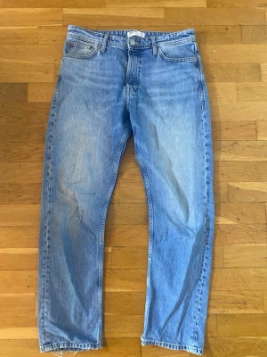Blå loose fit jeans från Jack & Jones - Säljer ett par ljusblå jeans från Jack & Jones med loose fit och klassisk femficksdesign. Jeansen har raka ben och är tillverkade i bomull. Perfekt för dig som gillar avslappnad stil och vill ha bekväma jeans med lite extra utrymme.