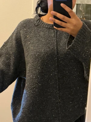 Mörkgrå stickad tröja från Bikbok - Säljer en mörkgrå stickad tröja från Bikbok i storlek M. Tröjan har ett diskret spräckligt mönster och en rak, loose passform med rund hals och långa ärmar. Perfekt för dig som gillar chill och enkel stil.