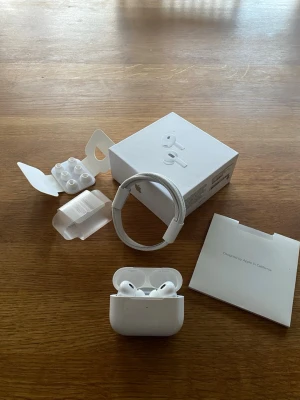 AirPods Pro gen 2 - Apple AirPods Pro med originalförpackning, extra öronkuddar, laddningskabel och manual. Trådlösa hörlurar med aktiv brusreducering och laddningsetui. Helt nya och aldrig använda.