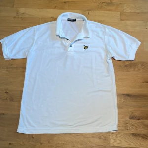 Vit pikétröja från Lyle & Scott - Vit pikétröja från Lyle & Scott Vintage med klassisk krage och korta ärmar. Tröjan har gul broderad logga på bröstet och knappar vid halsen. Materialet är tunn mjuk bomull. Den är liksom tunt stickad och så man ser igenom den lite. Storlek: S