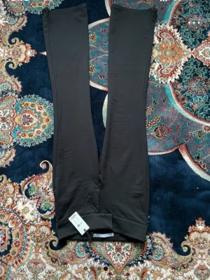 Svarta bootcut byxor från Vero Moda - Svarta bootcut byxor från Vero Moda med bred linning och stretchigt material. Snyggt utsvängda ben och enkel design utan synliga fickor eller detaljer. Perfekta för dig som gillar en stilren look och vill ha bekväma byxor med lite extra attityd.