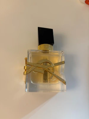 Trendig parfym med gulddetaljer - Snygg parfym från Yves Saint Laurent med ikonisk gulddetalj på flaskan. Perfekt för dig som vill ha en lyxig accessoar på sminkbordet. Volym och ingredienser syns ej på bilderna.