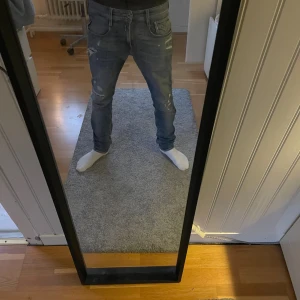 Replay blå jeans med slitningar - Säljer ett par snygga blå jeans från Replay med coola slitningar och detaljer på benen. Jeansen har normal passform och är tillverkade i jeansmaterial med en lite tvättad look. Perfekt för dig som gillar streetstyle och vill ha något som sticker ut.