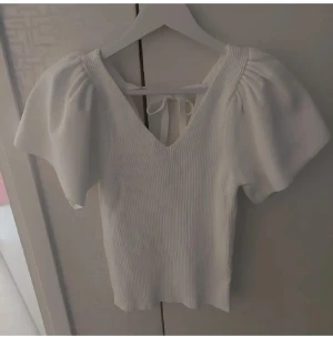 Vit ribbad topp från ONLY med puffärm och knytning i ryggen  - Säljer en ny vit ribbad topp från ONLY i storlek M. Toppen har puffiga korta ärmar, v-ringning fram och bak samt en knytning i ryggen. Köpt för 350kr. 🤍
