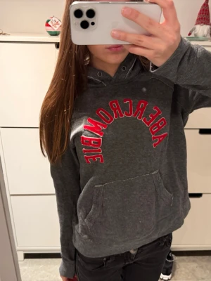 abercrombie & fitch hoodie huvtröja - Grå Abercrombie & fitch huvtröja med röd text. Storlek M!                                                                             Mycket bra skick, bara dragskon som saknas.