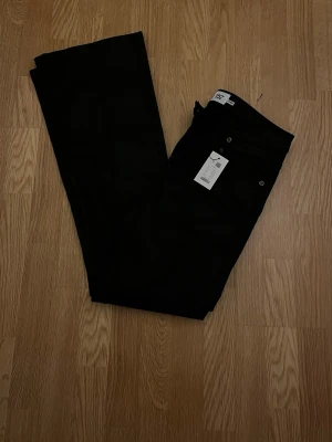 Svarta skinn byxor från 157 - Snygga svarta byxor från 157 med bootcut-snitt och mid Waits. Materialet har en glansig finish som ger en cool look. Klassisk femficksmodell med knapp och dragkedja framtill. Perfekta för dig som gillar stilrena och trendiga byxor.