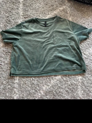 Grön croppad t-shirt från Brandy Melville - Säljer en chill grön t-shirt från Brandy Melville i mjuk bomull. Modellen är croppad med korta ärmar, rund hals och en ficka på bröstet. Perfekt för dig som gillar loose fit och enkel stil. Slits i sidorna för extra vibe.