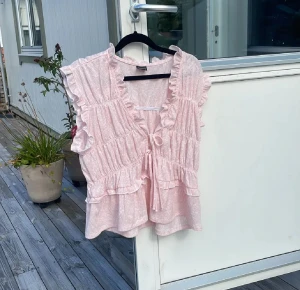 Rosa tröja/bluss - Ljusrosa tröja från Ginatricot i storlek L. Tröjan har en feminin design med volanger vid ärmhålen och halsringningen samt knytning framtill. Smockad/rynkat tyg som ger en fin passform och lätt utsvängd nederdel. Mjukt och luftigt material, perfekt för vår och sommar. I gott skick.