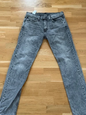 Levi's 501 grå jeans straight fit - Säljer ett par Levi's 501 jeans i grå tvättad färg med klassisk straight fit. Jeansen har fem fickor, knappgylf och Levi's patch baktill. Materialet är robust denim i bomull och passformen är normal. Perfekt för dig som gillar tidlös stil och vill ha ett par snygga jeans.