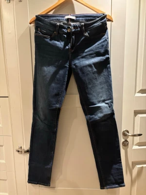 Tommy Hilfiger Milan slim jeans blå - Snygga blå jeans från Tommy Hilfiger, modell Milan med slim fit och klassisk femficksdesign. Jeansen har orangea sömmar, läderpatch med logga och är tillverkade i mjukt jeansmaterial. Perfekt passform med smal siluett och normal midja.