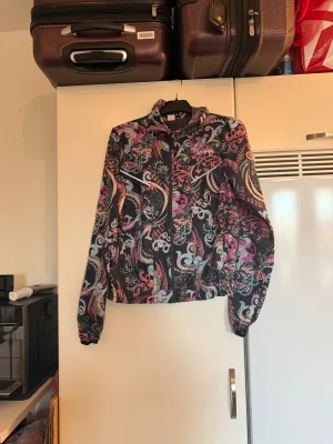 Mönstrad vindjacka från Odd Molly - Säljer en färgstark vindjacka från Odd Molly med coolt paisley-inspirerat mönster i rosa, blått, lila och svart. Jackan har dragkedja framtill, huva och elastiska muddar. Perfekt för dig som gillar att sticka ut med din stil. Storlek 1 som enligt deras storleksguide motsvarar en S. men måttet armhåla till armhåla är 50cm.  Mycket fint skick, jag hittar inga synliga anmärkningar eller defekter.  