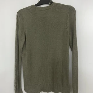 Olivgrön stickad tröja från Lindex - Snygg olivgrön stickad tröja från Lindex med flätstickade detaljer framtill och längs ärmarna. Tröjan har rund halsringning, ribbade muddar och lång ärm. Perfekt för lager-på-lager under kyliga dagar.