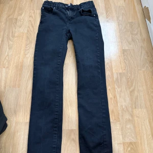 Svarta jeansbyxor från 157, stl 160 - Svarta jeansbyxor från 157 med klassisk femficksdesign och rak passform. Byxorna har resår i midjan för extra komfort och är tillverkade i ett mjukt bomullsmaterial. Perfekta för dig som gillar en enkel och stilren look.