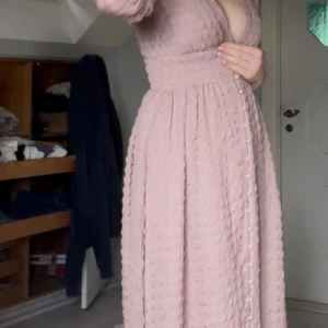 Ljusrosa klänning med knappar - Säljer en ljusrosa långklänning med djup v-ringning och puffiga trekvartsärmar. Klänningen har ett markerat midjeparti och dekorativa knappar längs hela framsidan. Materialet är strukturerat och väldigt skönt. Säljes då den är lite kort för mig som är 172. Passar bra för någon som är typ 165. Från Na-kd, nypris runt 900. Säljer för 350🥰