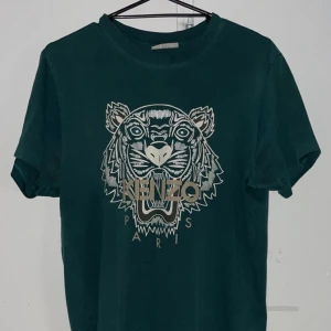  Kenzo t-shirt med tigertryck - Kom med pris. Mörkgrön t-shirt från Kenzo i bomull med ikoniskt tigertryck och Kenzo Paris-logga framtill. Klassisk rund hals och korta ärmar. Perfekt för dig som vill sticka ut med en streetstyle-vibe.