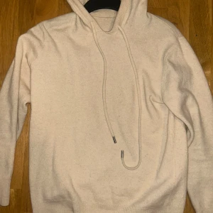 Beige hoodie med huva och snörning - Mysig beige hoodie med huva och långa ärmar. Tröjan har snörning med metalländar och ribbade muddar vid ärmslut och nederkant. Perfekt för dig som gillar en enkel och stilren look.