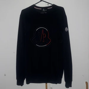 Moncler sweatshirt med logga - Kom med pris. Säljer nu denna mocler pågrund av att den är för stor det är en svart sweatshirt från Moncler Grenoble med stor broderad logga på bröstet och klassisk Moncler-patch på ärmen. Tröjan har rund halsringning, långa ärmar och ribbade muddar. Perfekt för dig som gillar stilrena och exklusiva plagg.