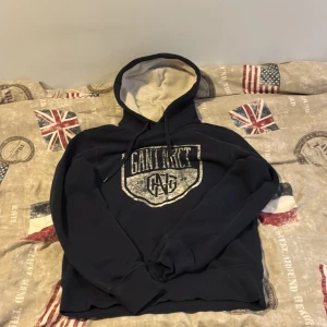 Mörkblå hoodie från GANT med tryck - Säljer en mörkblå hoodie från GANT med stort vitt tryck framtill och snörning i huvan. Insidan av huvan är ljus och tröjan har ribbade muddar. Perfekt för dig som gillar klassisk stil.  Storlek s men passar även xs.         Är lite använd men syns knappt😀kan gå ner i pris vid snabb affär, hör av er vid funderingar 