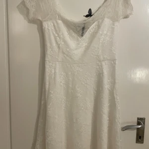 Vit spetsklänning från Bubbleroom - Superfin vit klänning från Bubbleroom med spetsdetaljer och offshoulder-ärm. Klänningen har v-ringning och är figursydd upptill med lätt utsvängd kjol. Perfekt för sommarens alla tillfällen när du vill känna dig extra söt och romantisk.