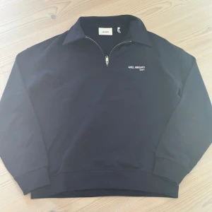 Svart half zip-tröja Axel Arigato M - Mörk blåtröja från Axel Arigato med halv dragkedja och liten vit logga på bröstet. Klassisk krage och långa ärmar. Perfekt för en clean och stilren look. M