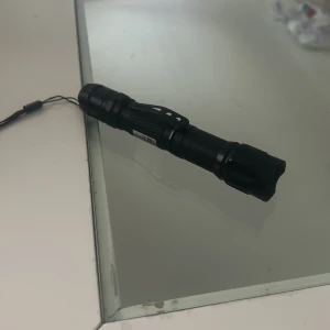 Grön laserpekare med laddare - Kraftfull grön laserpekare i svart metallhölje, levereras med handledsrem och laddare. Produkten är i gott skick och fungerar utmärkt, vilket syns på bilderna. Perfekt för presentationer, astronomi eller hobbybruk.