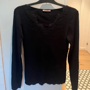 Svart ribbad topp med spets från Anna Field - Svart långärmad topp från Anna Field i ribbat material. V-ringning och spets. Använd 2-3 gånger och har därför fortfarande väldigt bra skick. Säljer pga för stor för mig. 