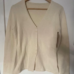 Beige kofta med v-ringning och knappar - En stilren beige kofta med v-ringad hals och knäppning framtill. Koftan har långa ärmar och är tillverkad i ett mjukt, stickat material som känns skönt mot huden💛