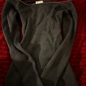 Ribbad grå offshoulder tröja - Snygg ribbad grå tröja med offshoulder-modell och långa ärmar. Klänningen har pärldetaljer längs halsringningen och är figurnära med stretchigt material. Perfekt för dig som gillar en stilren och trendig look.