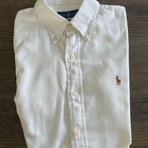 Klassisk skjorta från Ralph Lauren - Säljer en stilren skjorta från Ralph Lauren med klassisk krage och knäppning framtill. Skjortan har lång ärm och ikonisk broderad logga på bröstet. Finns i vitt och ljusblått, tillverkad i mjuk bomull. Perfekt för dig som gillar en clean och tidlös look. Den turkosa har liten fläck på ena ärmen