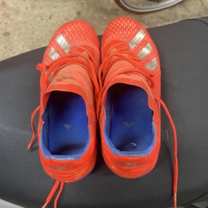 Röda Adidas fotbollsskor med silverdetaljer - Säljer ett par röda Adidas fotbollsskor med silvriga ränder på sidorna och blå innersula. Jag kan tvätta skorna om ni vill