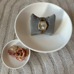 Martyn Line klocka i silver och guld - Snygg klocka från Martyn Line med tvåfärgad länk i silver och guld. Urtavlan är silverfärgad med romerska siffror och ramen är dekorerad med glittrande stenar. Klassisk och stilren design som sticker ut med sina detaljer.