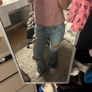 Hollister Jeans - Säljer ett par ljusblå jeans med bootcut-modell och stora slitningar på båda benen. Jeansen har klassisk femficksdesign, låg midja och är tillverkade i denim. Perfekta för dig som gillar en avslappnad och trendig look. Pris kan disskuteras
