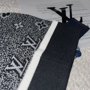 Svartvit mössa - Exklusiv svartvit mössa med klassiskt monogram och logotyp framtill. Stickad i mjukt material med bred, svart kant och vit rand. Perfekt accessoar för dig som vill sticka ut med lyxig streetstyle.