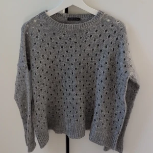 Grå stickad prickig tröja Italy - Grå stickad tröja med prickigt hålmönster från Made in Italy. Tröjan har rund halsringning, ribbade muddar och lång ärm. Perfekt för dig som gillar en mysig och trendig look med lite oversized känsla.