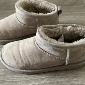 Beige UGG  - Säljer ett par klassiska UGG boots i beige mocka med mjukt och fluffigt pälsfoder på insidan. Skorna har rund tå, platt sula och låg skaft. Perfekta för kalla dagar och har en stilren look med UGG-logga bak på hälen.