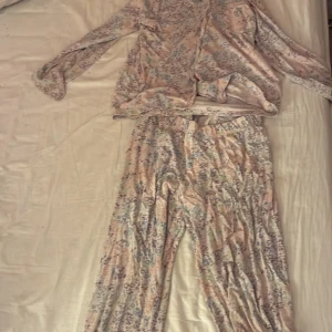 Blommiga pyjamasbyxor från Kappahl - Supersköna pyjamasbyxor från Kappahl i storlek 134/140. Byxorna har ett blommigt mönster i pastelliga färger som lila, rosa och blått. De är vida och har resår i midjan för extra komfort. Perfekta för mysiga hemmakvällar!