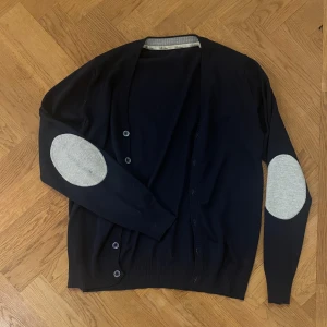 Stenströms kofta - Säljer min mörkblåa kofta från Stenströms med grå armbågslappar och ribbad grå kant vid halsen. Koftan har knappar framtill och är långärmad. Perfekt för lager-på-lager och snygg till både jeans och chinos.